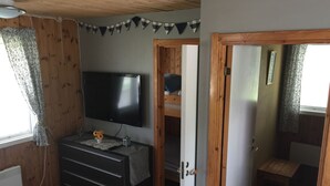 A room with a TV on a dresser, a wooden door, and a view into another room.