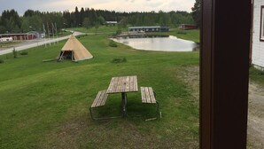 A grassy area with a picnic table, a teepee, a small pond, and buildings in the background.