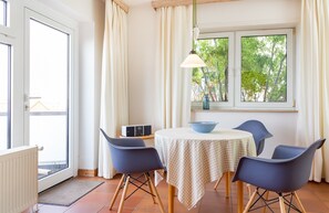 Ein Essbereich mit Tisch, Stühlen, einer Schüssel und einem Fenster mit Vorhängen.