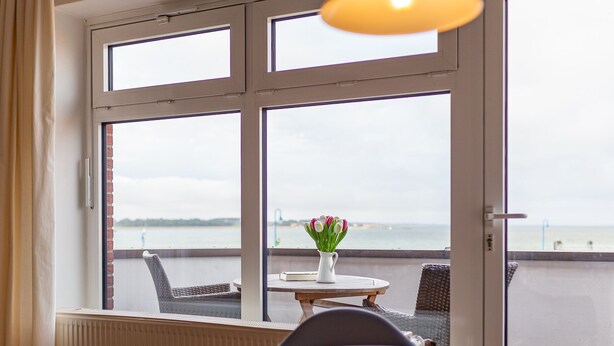 A room with a view of the sea through large windows, a table with a vase of flowers, and a chair. - Fantastic holiday apartment with beautiful views to the sea, it is dog friendly (Wittdün)