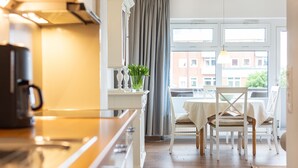 A modern kitchen with a coffee maker, a dining area with a table and chairs, and a view of a building through a window. - Wonderful holiday flat with ocean view to the island Amrum - Seaview, Dogfriendl (Wittdün)