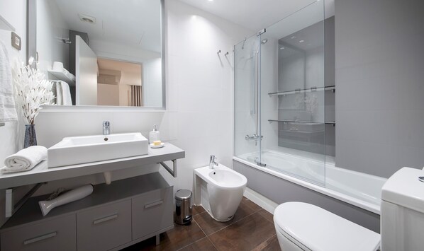 Un baño moderno con lavamanos blanco, espejo y cabina de ducha de vidrio.