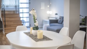 Un comedor moderno con una mesa redonda, sillas blancas, un jarrón con flores blancas y velas.