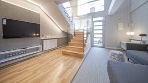 Una sala de estar moderna con un televisor de pantalla plana, suelo de madera, una escalera y un sofá gris.
