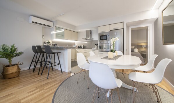 Uma cozinha moderna com uma ilha central, banquetas brancas e uma mesa de jantar com cadeiras.