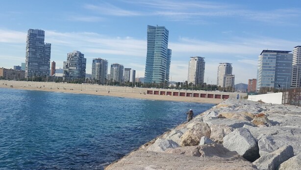 Un paisaje urbano costero con modernos edificios altos, una playa arenosa y terreno rocoso.