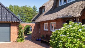 Une maison en briques avec un toit de chaume, une arche en briques et une allée pavée.