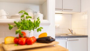 Une cuisine avec des meubles blancs, un plan de travail muni d’une planche à découper et divers ustensiles de cuisine.