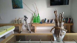 A room with a glass table, a tripod, a bookshelf, and a TV mounted on the wall. - Hotel Esperos (Skiathos)
