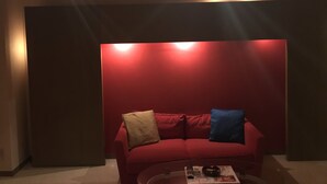 Un sofá rojo con dos cojines, una mesita de centro con un control remoto y una revista, y una pared de acento roja.