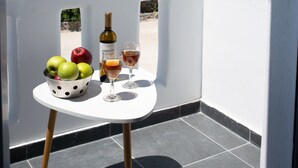 Un balcón con una mesa que sostiene una botella, dos vasos y un cuenco de fruta. Se divisa un crucero en el fondo.