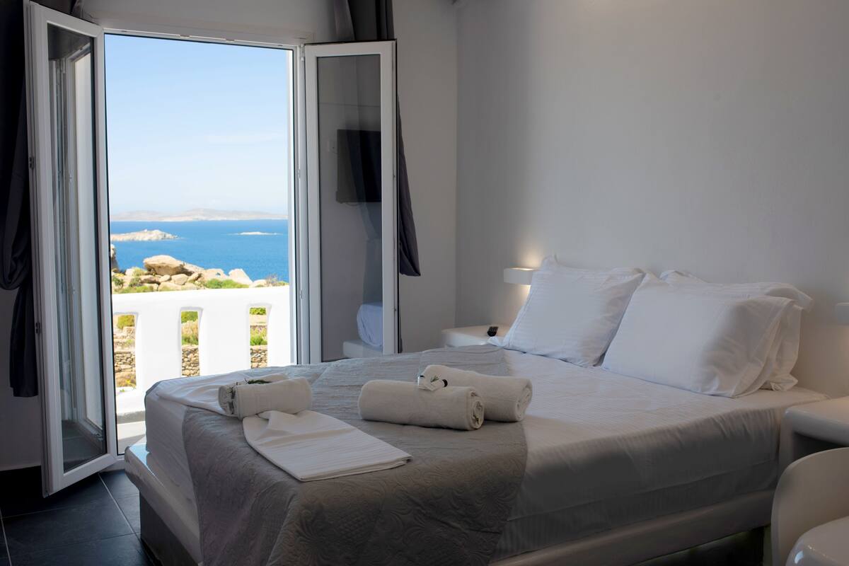 Een slaapkamer met een bed, een nachtkastje, een televisie en uitzicht op zee.