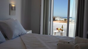 Habitación de hotel con una cama grande, una mesita con una botella y vasos, y vista a la playa y al océano.