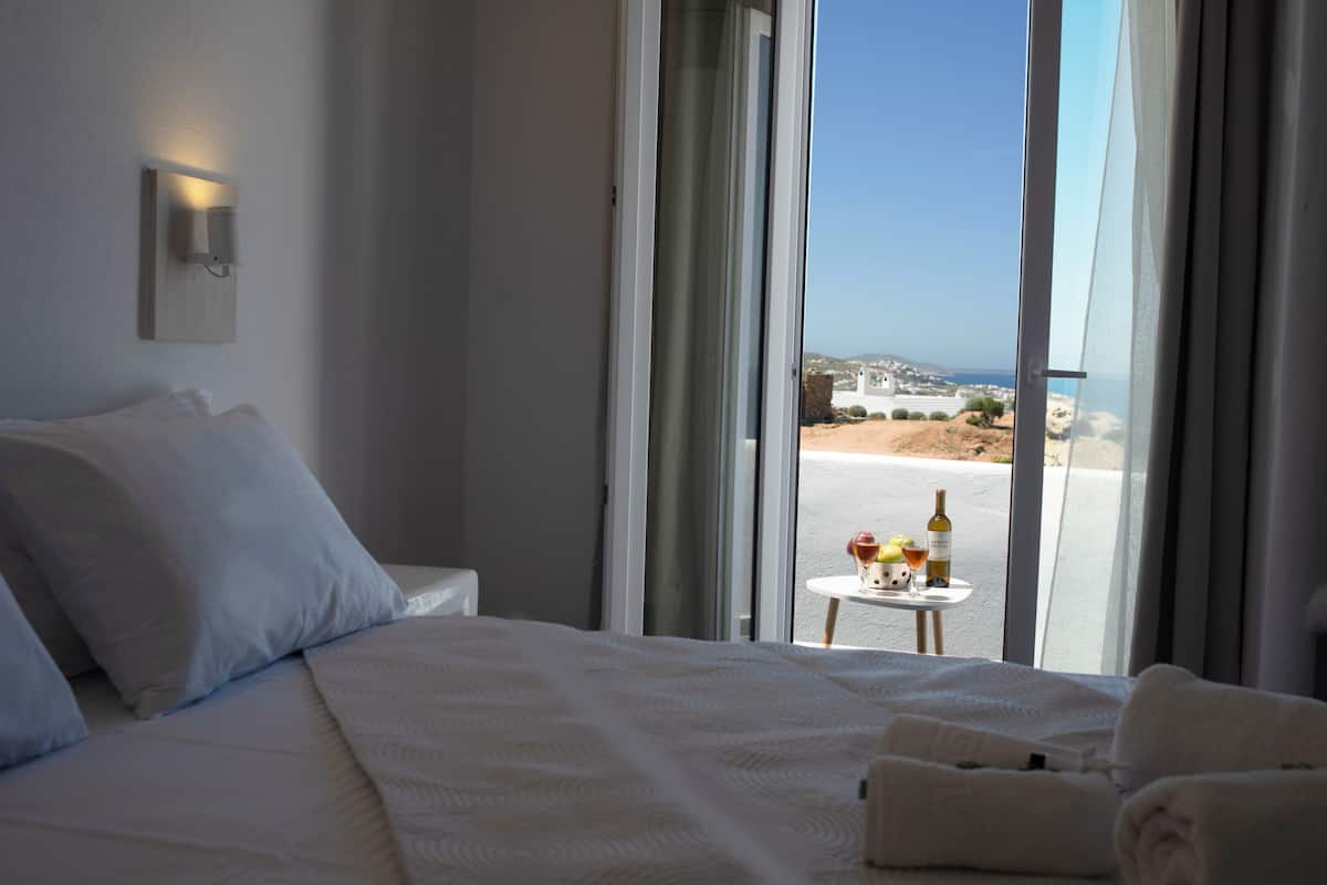 Een hotelkamer met een groot bed, een klein tafeltje met een fles en glazen, en uitzicht op het strand en de oceaan.