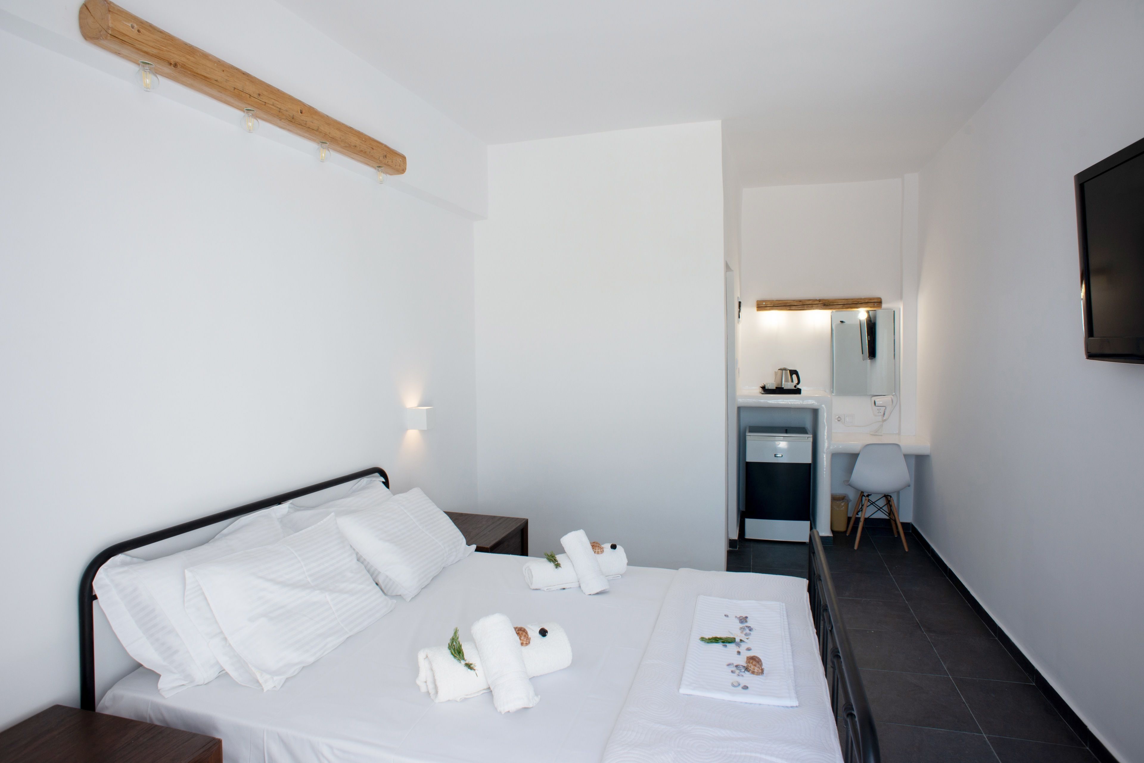A hotel room with a bed, a wooden headboard, a nightstand, a desk with a chair, a mirror, and a television.