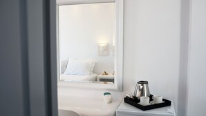 Una habitación de hotel con una cama, una mesita de noche con cafetera, tazas y una bandeja.