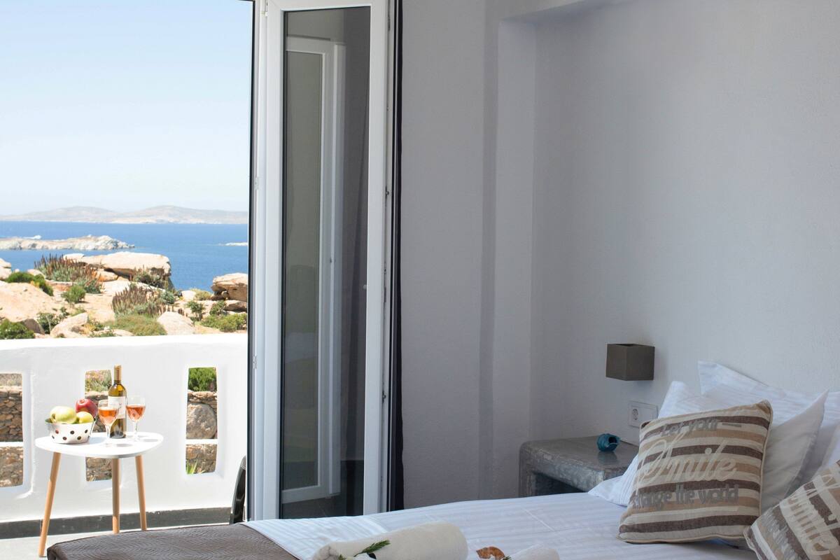 Een slaapkamer met een bed, een nachtkastje, een raam met uitzicht op zee en een airconditioning.