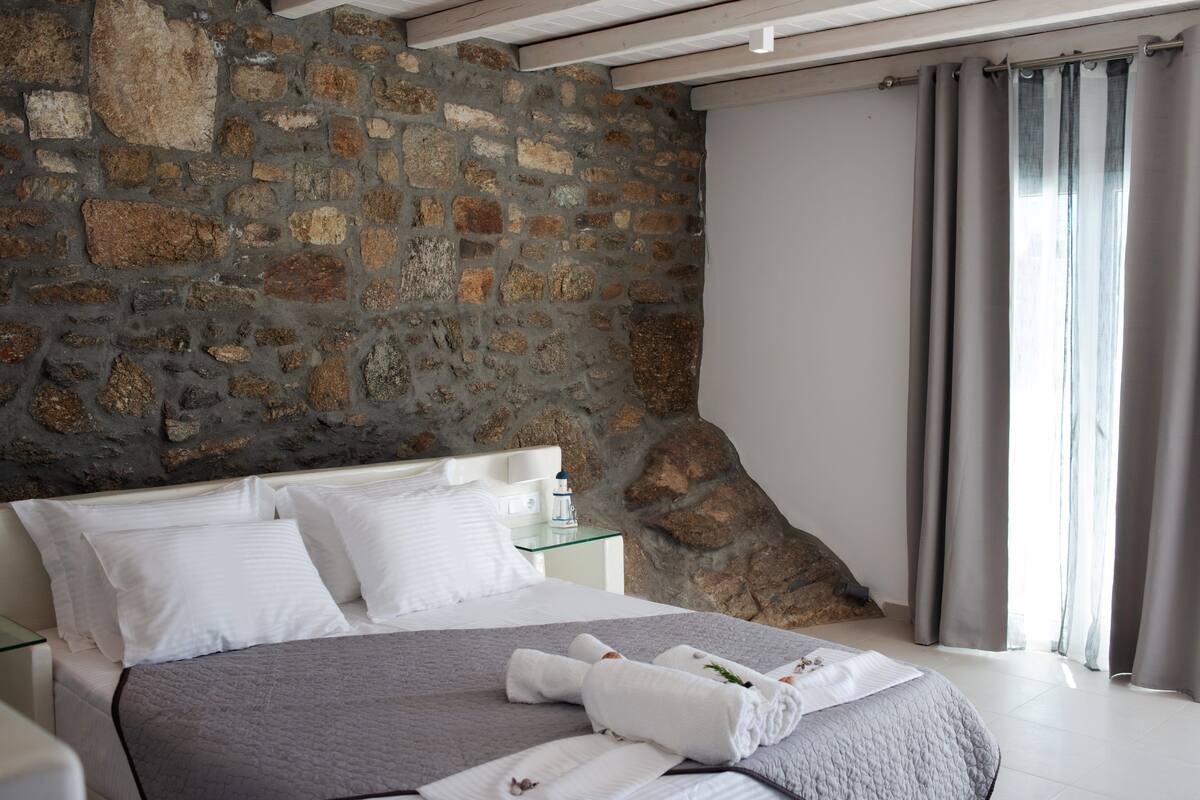Een slaapkamer met een stenen muur, een bed met witte beddengoed en een glazen nachtkastje.