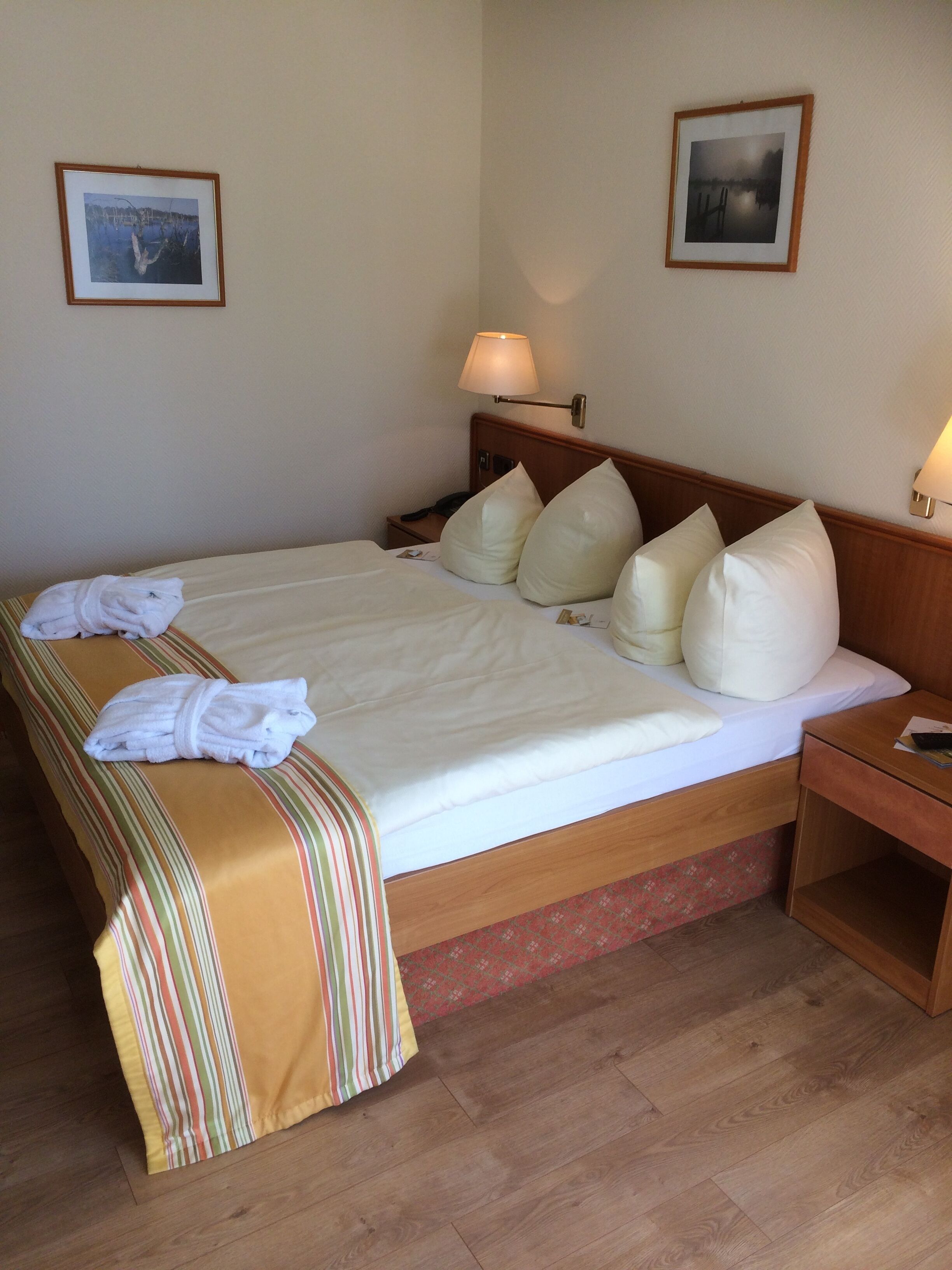 Ein Hotelzimmer mit einem großen Bett, zwei Kissen, einem Nachttisch, einer Lampe und zwei gerahmten Bildern an der Wand.