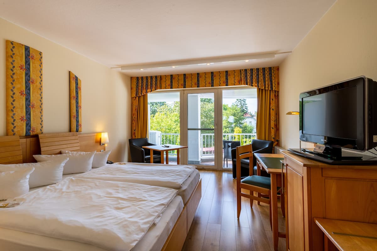 Ein Hotelzimmer mit zwei Betten, einem Schreibtisch mit Fernseher und einem Balkon mit Tisch und Stühlen.