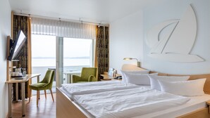 A hotel room with a large bed, a desk, a chair, and a view of the sea. - Seehotel Fährhaus (Bad Zwischenahn)