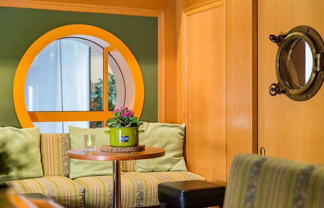 Una habitación acogedora con un ventanal redondo, una pequeña mesa con una planta en maceta y una puerta de madera con un espejo redondo.