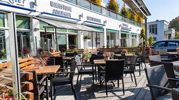 Ein Außenbereich mit Tischen und Stühlen, einer Holzterrasse und einem Gebäude mit Beschilderung.