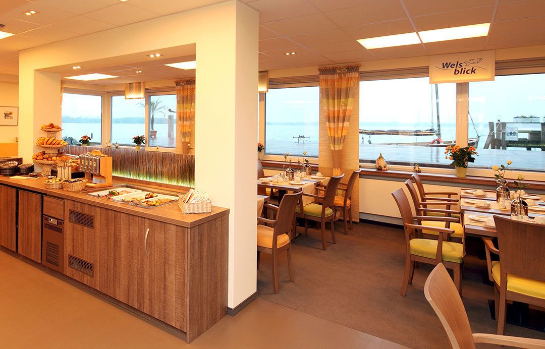 A restaurant with a buffet area, wooden furniture, and a view of the sea.