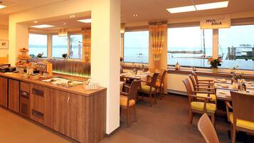 A restaurant with a buffet area, wooden furniture, and a view of the sea.