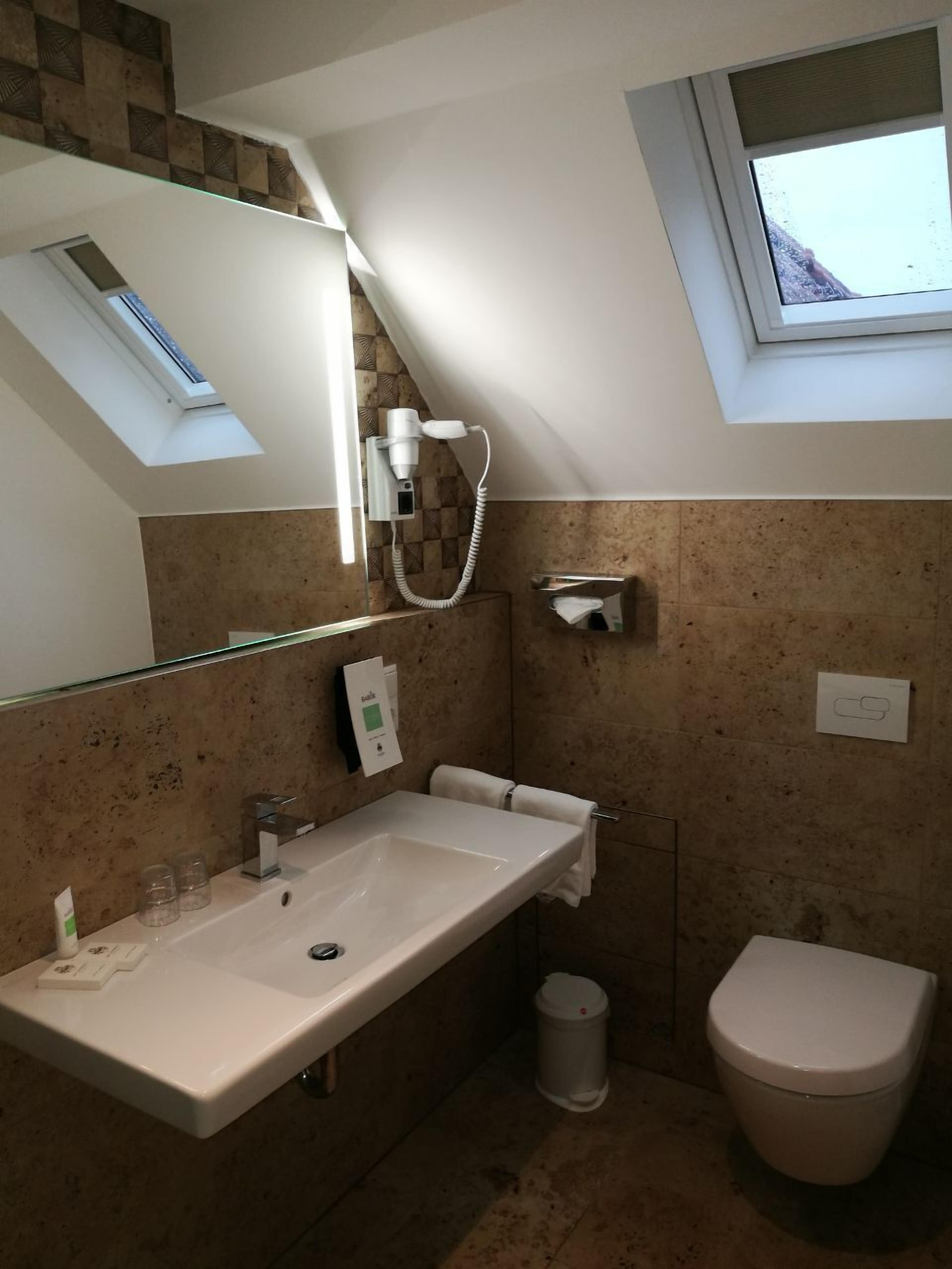 Een moderne badkamer met dakraam, grote spiegel, wastafel, toilet en handdoekhouder.