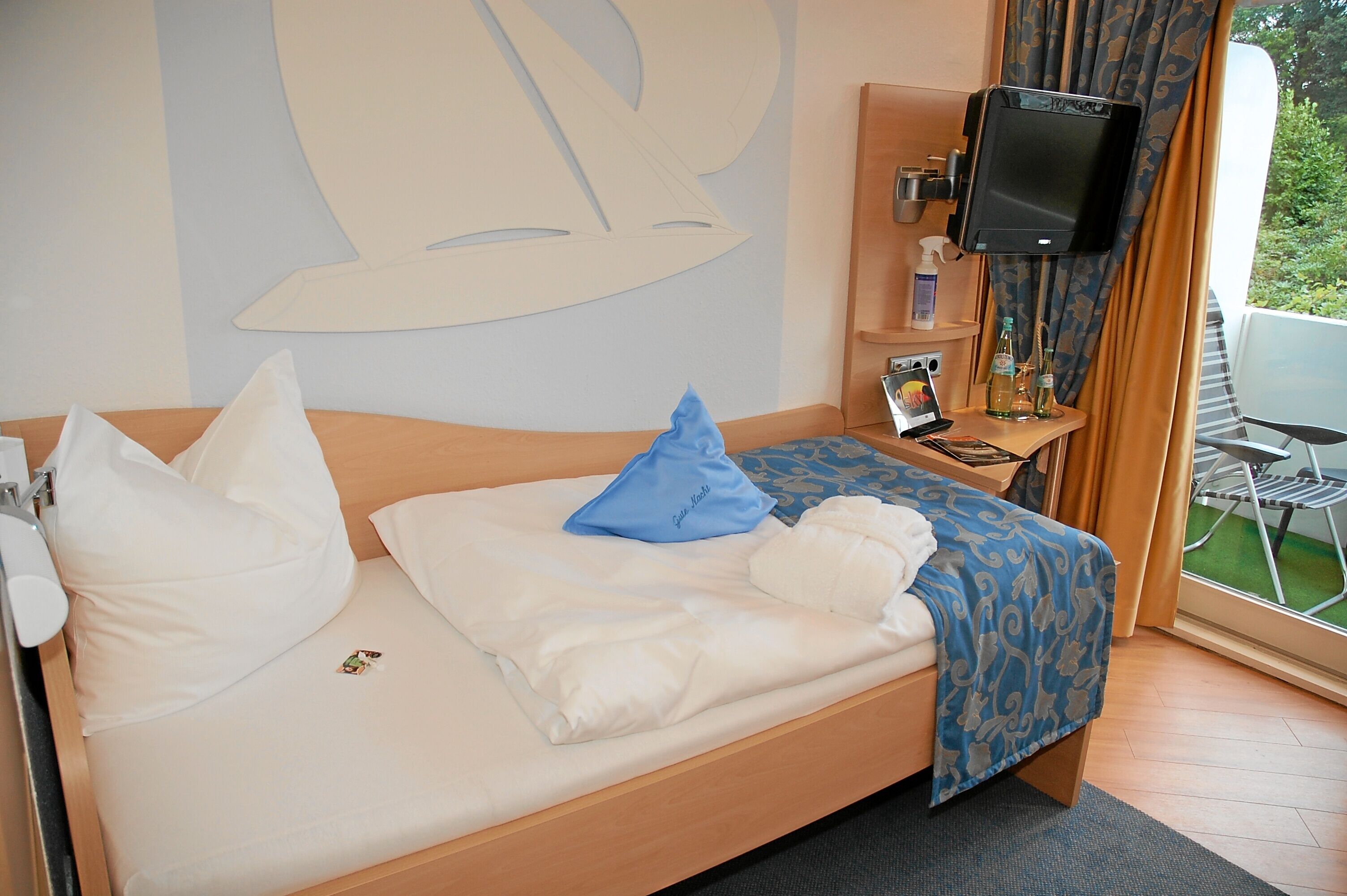Habitación de hotel con cama, televisor, una mesita con botellas y vistas al verdor exterior.