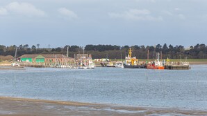 Ein Hafen mit vertäuten Booten, ein grünes Gebäude und eine Mole, die sich ins Wasser erstreckt.