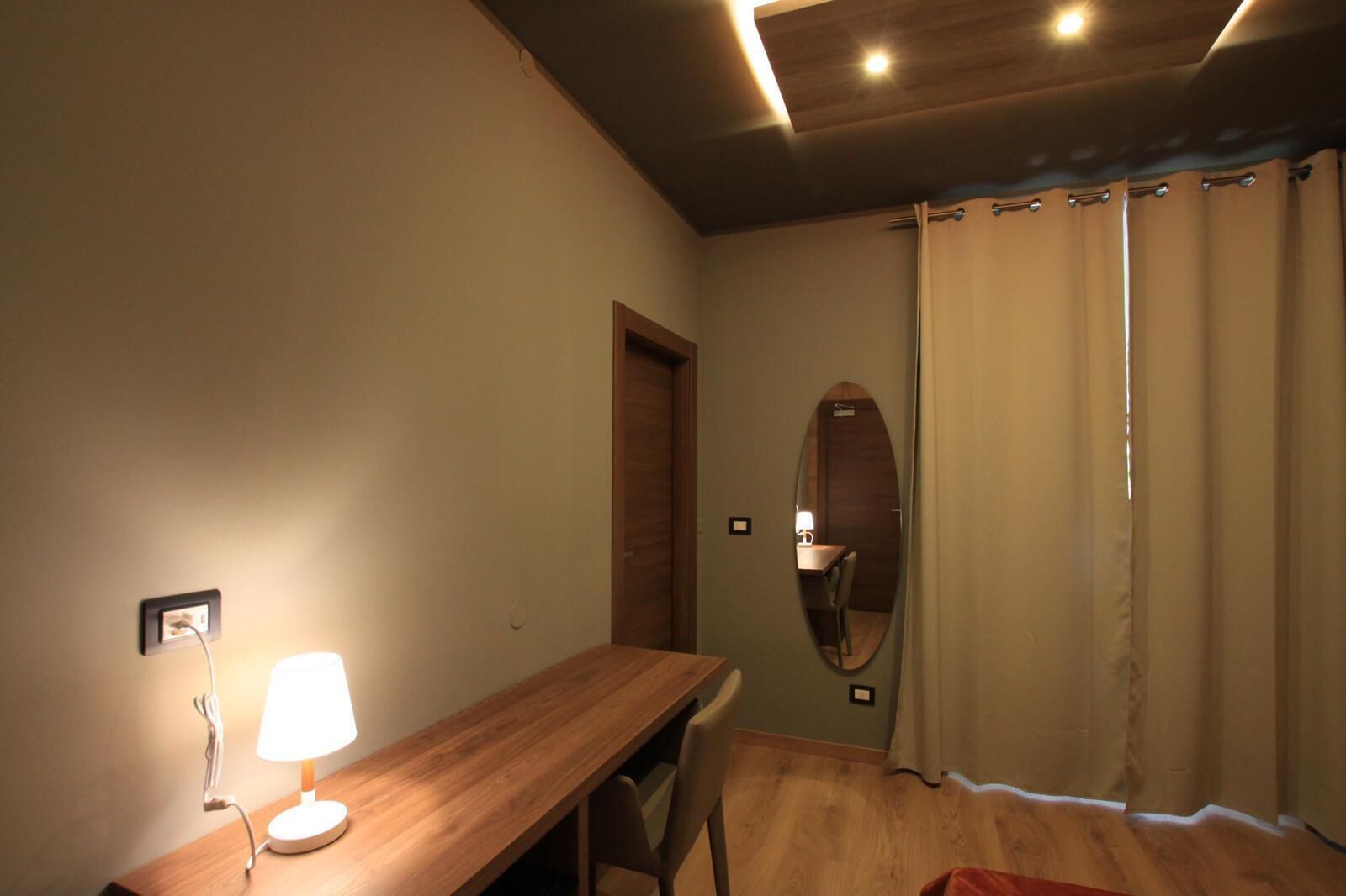 Een kamer met een houten bureau, een lamp, een spiegel en een deur.