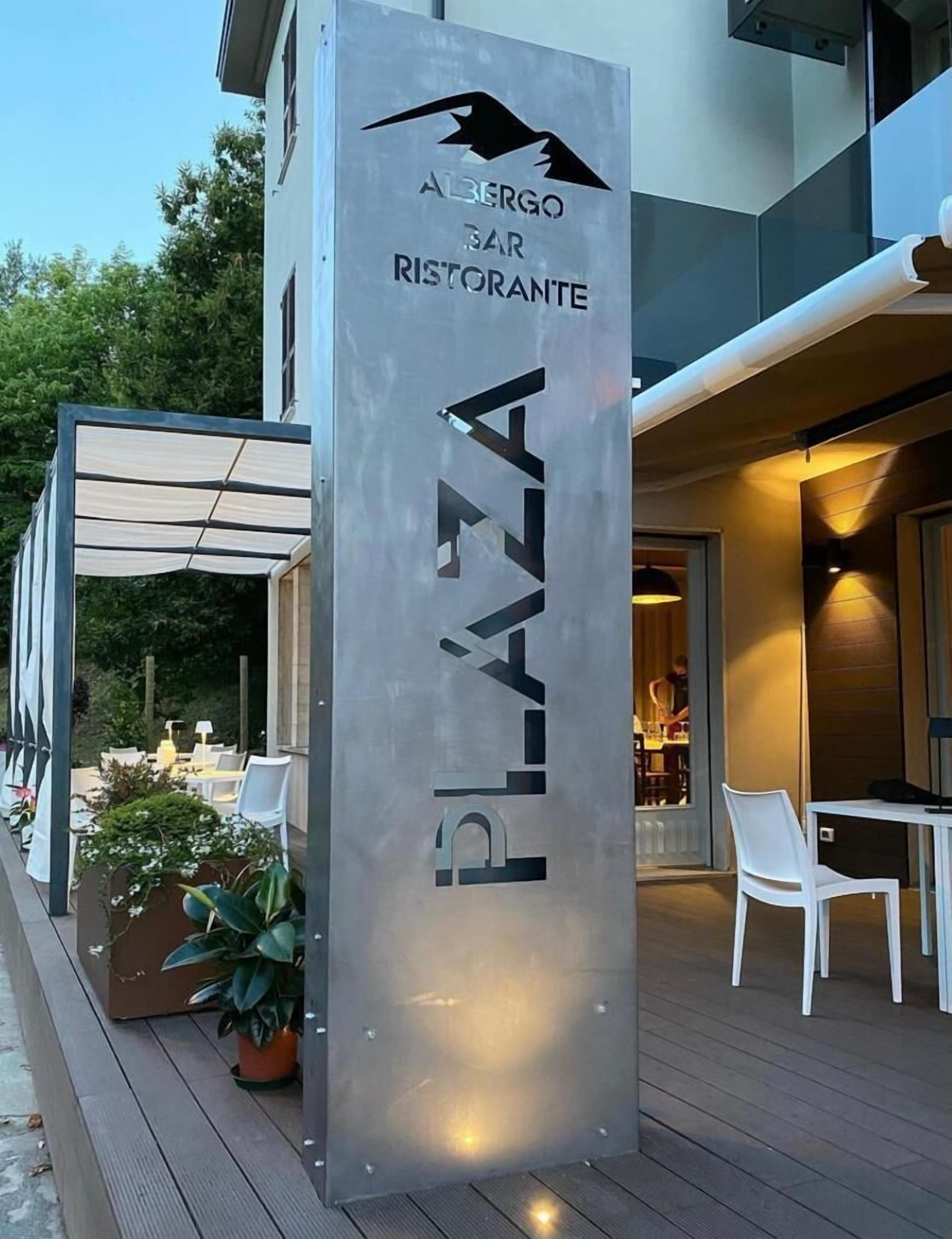 Un edificio moderno con un letrero que dice 'ABERGO SAR RISTORANTE PLAZA' y un área de estar al aire libre.