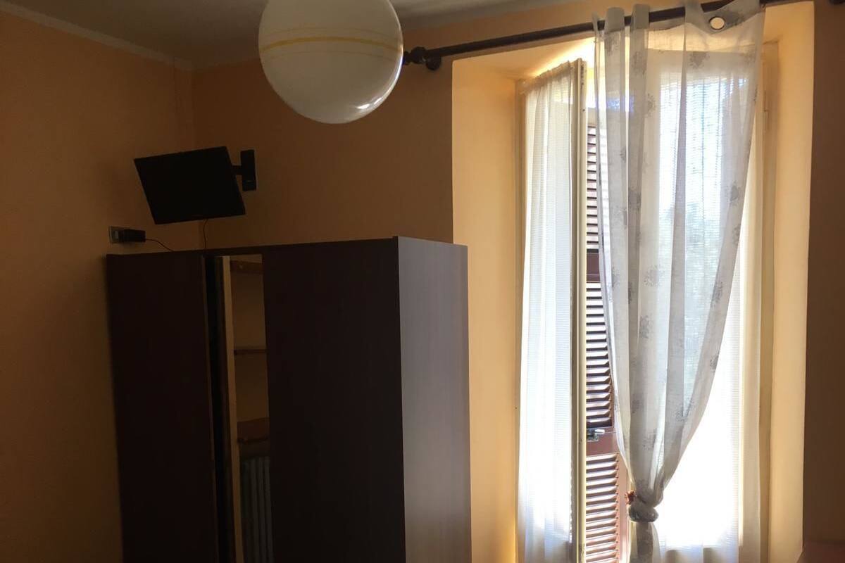 Habitación de hotel con cama, armario, espejo, luz de techo y ventana con cortinas.