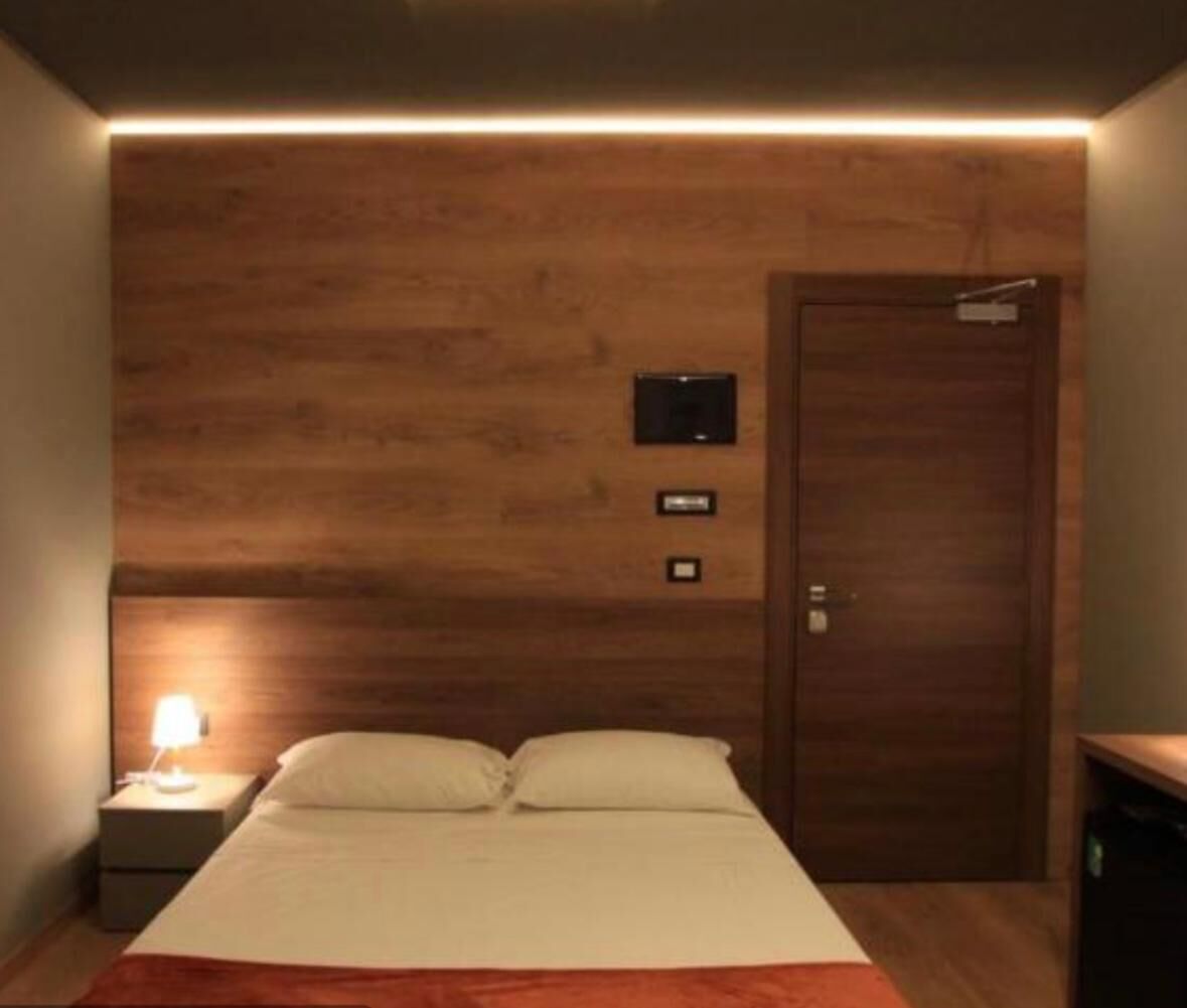 A bedroom with a wooden headboard, a bed with white bedding, a nightstand with a lamp, and a door with a sign above it.