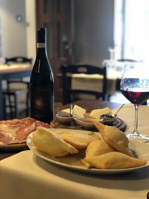 A dining table with a plate of food, a bottle of wine, and a glass of red wine. - Albergo Plaza Tornolo (Tornolo)