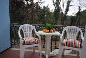 Two white chairs with striped cushions on a balcony with a table in the center, surrounded by a railing. - Villa Tiziano (Lignano Sabbiadoro)