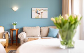 Un salon avec un canapé, une petite table sur laquelle est posé un vase de fleurs, un tableau au mur et une lampe.