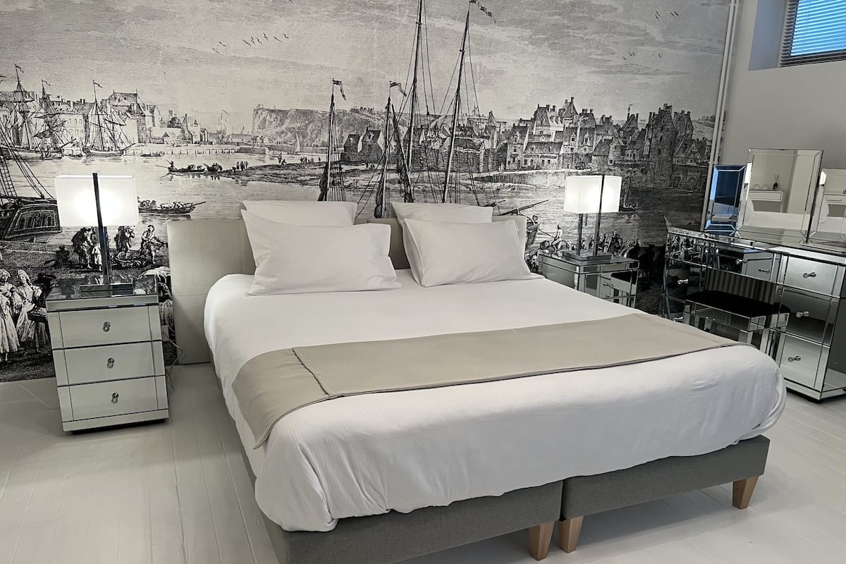 Un dormitorio moderno con una cama grande, dos mesitas de noche y un mural de un pueblo costero.