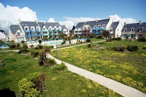 Um hotel com piscina, um jardim com flores amarelas e um caminho.