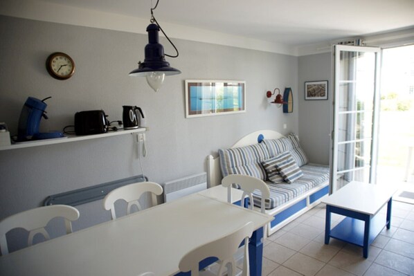 Um quarto com uma mesa de jantar, cadeiras, um sofá com almofadas listradas, um relógio na parede e uma janela com vista.