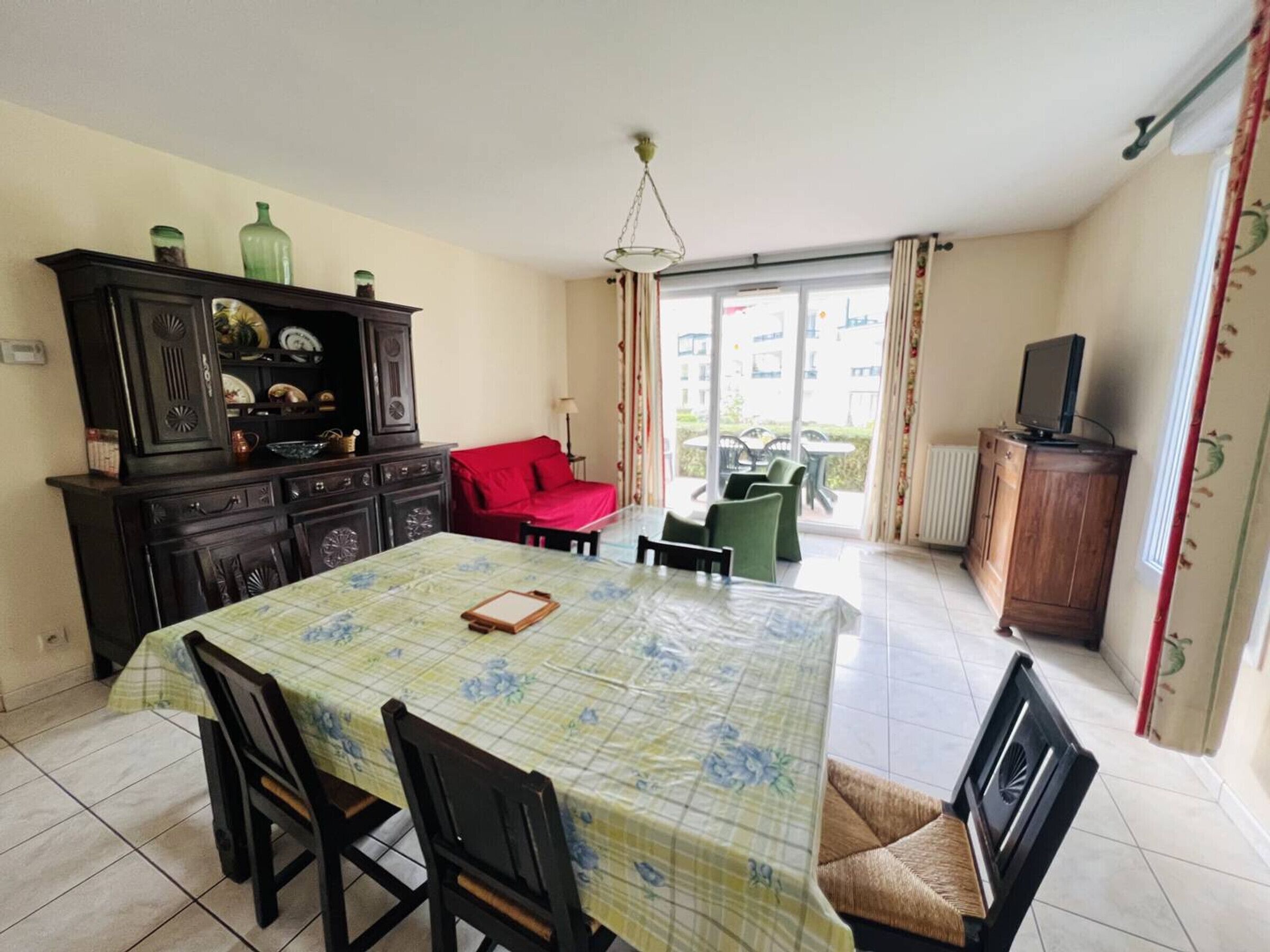 A dining area with a table set for four, a red sofa, and a television on a wooden cabinet.
