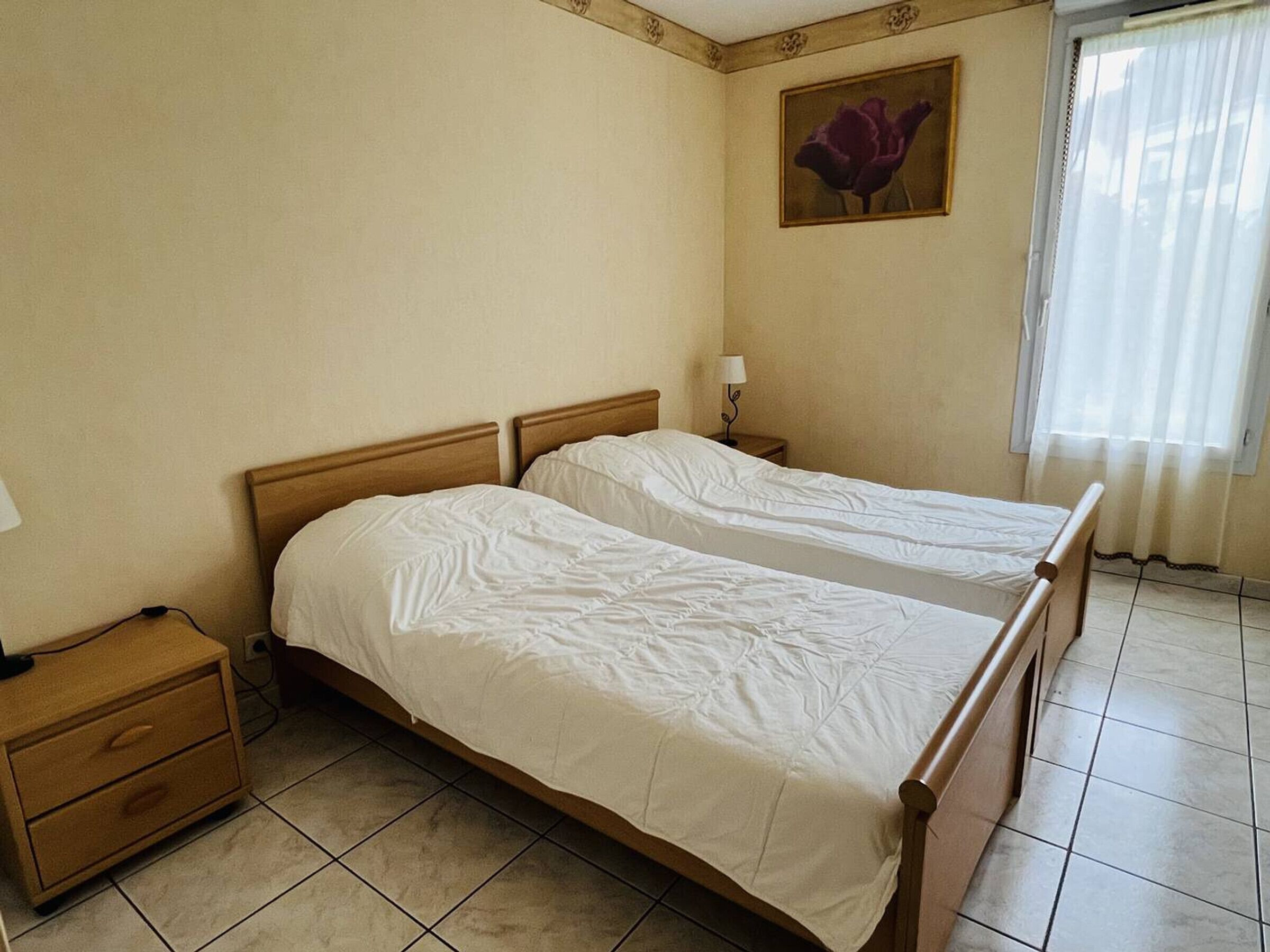 Una habitación de hotel con dos camas individuales, una mesita de noche, una lámpara y un cuadro en la pared.