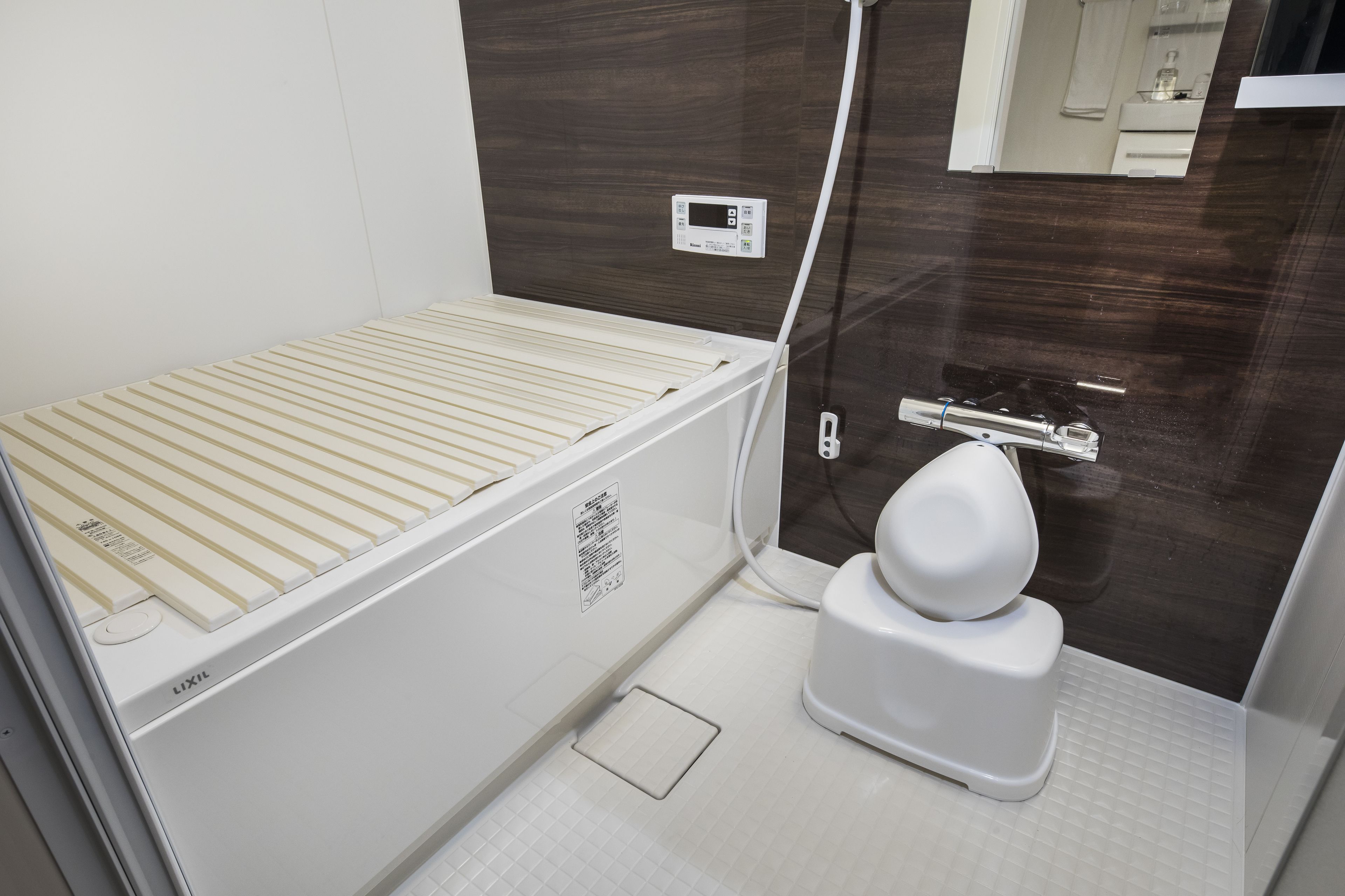 A compact bathroom with a white toilet, a shower area, and a control panel on the wall.