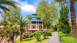 Un edificio de estilo tradicional con techo azul, rodeado de exuberante vegetación y palmeras.