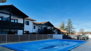Zona residencial con un lona azul grande cubriendo un espacio exterior, posiblemente una piscina o patio, rodeada por una cerca blanca y casas contiguas con balcones.