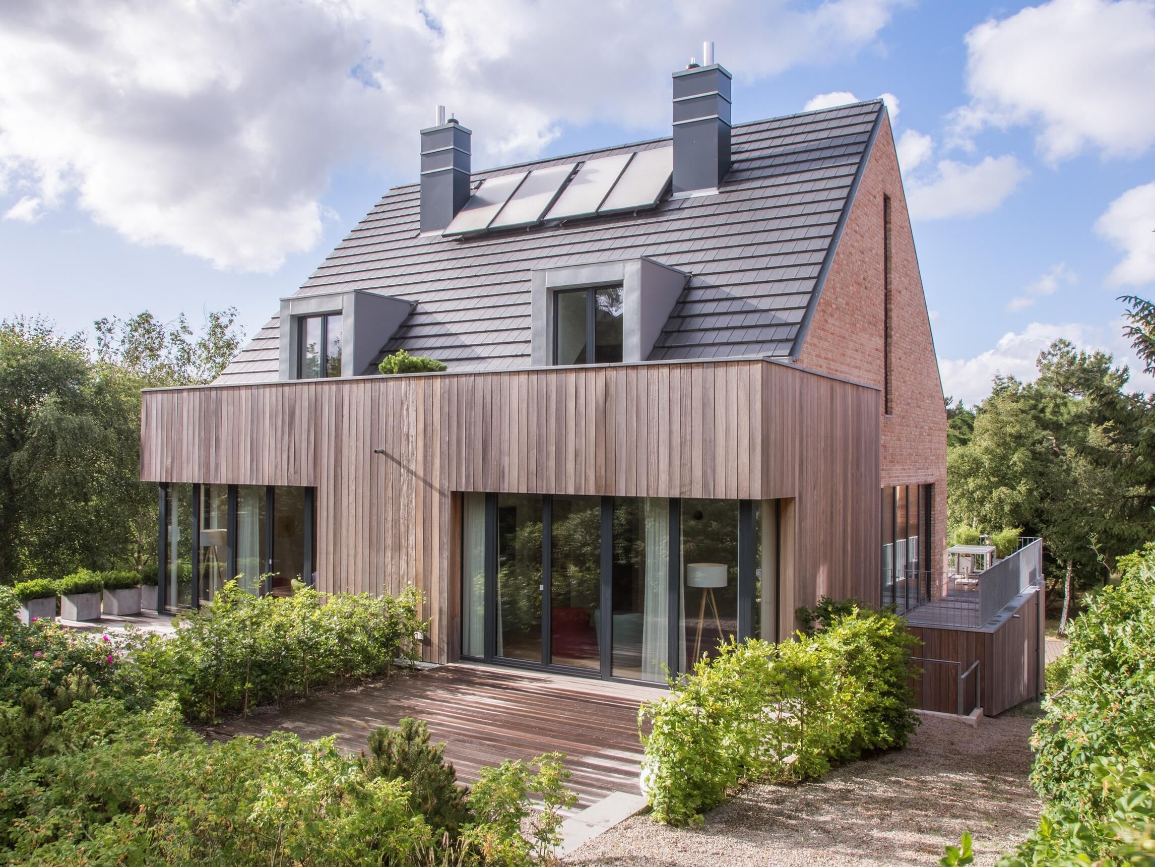 Ett modernt hus med ett sluttande tak, stora fönster och en träaltan.
