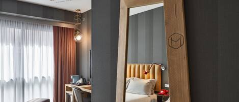 A modern hotel room with a large mirror, a desk, a comfortable bed, and a view of the city.