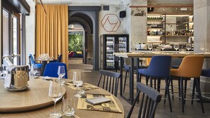 A restaurant with a bar area, dining tables, and chairs. There are wine glasses and bottles on the tables.
